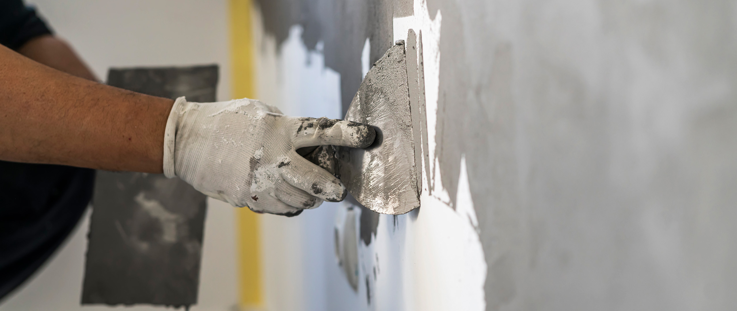 Hånd i arbejdshandske spartler en væg.